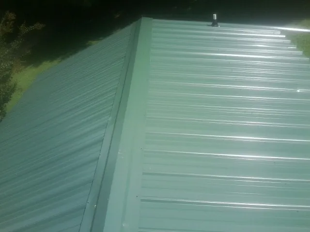 New green metal panels meeting at the ridge of a roof — Flat Roof Repair work by our crew in Wood Dale