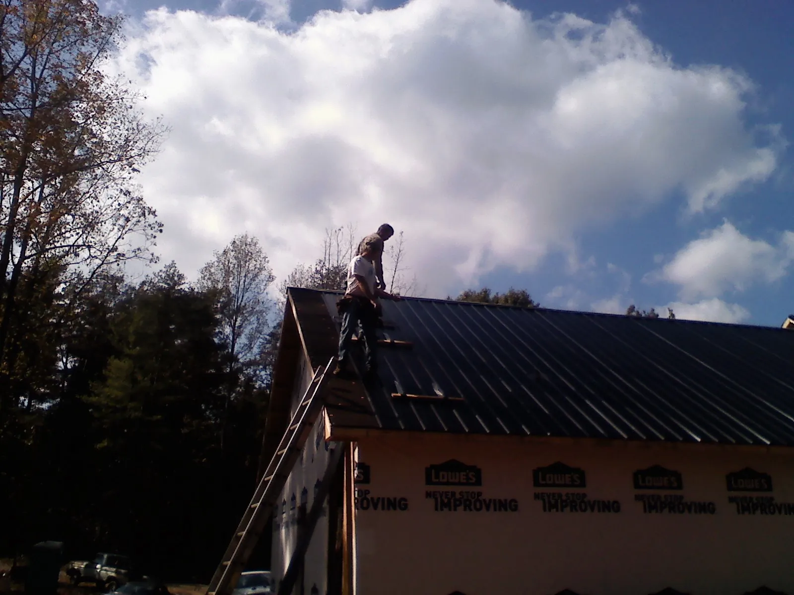 Roofer fastening dark metal panels high against a cloudy sky, from a Roof Inspection job in Wood Dale