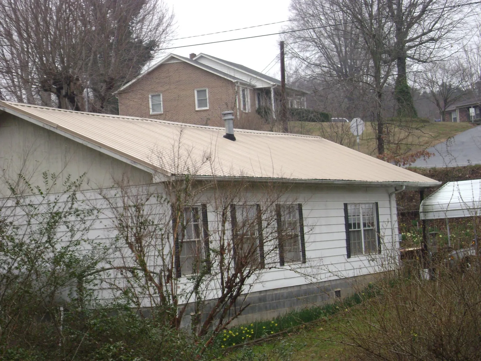 Tan metal roof on a white sided house set into a hillside — Commercial Roofing by Roofing Brothers in Wood Dale